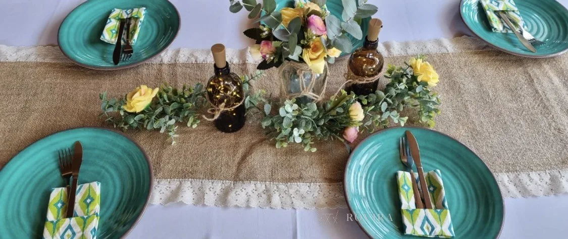 Puesto de mesa rústico en turquesa: platos turquesa, camino de yute con encaje, centro de eucalipto, rosas amarillas y botellas de vidrio con luces