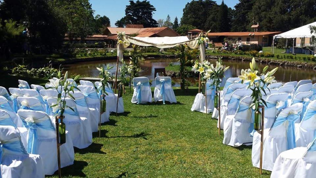Ceremonia junto a laguna, sillas blancas con lazo celeste y arreglos de lirios