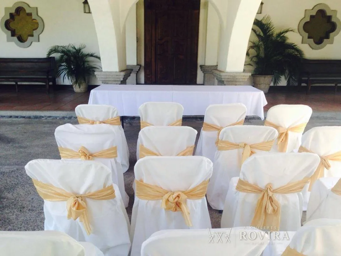 Sillas forradas blancas con lazo dorado, arquitectura estilo hacienda colonial