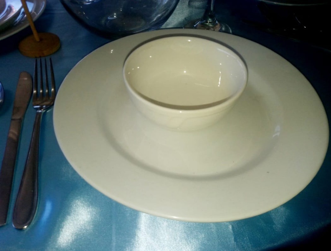Plato base plateado con vajilla blanca apilada y taza, sobre mantel estampado cebra