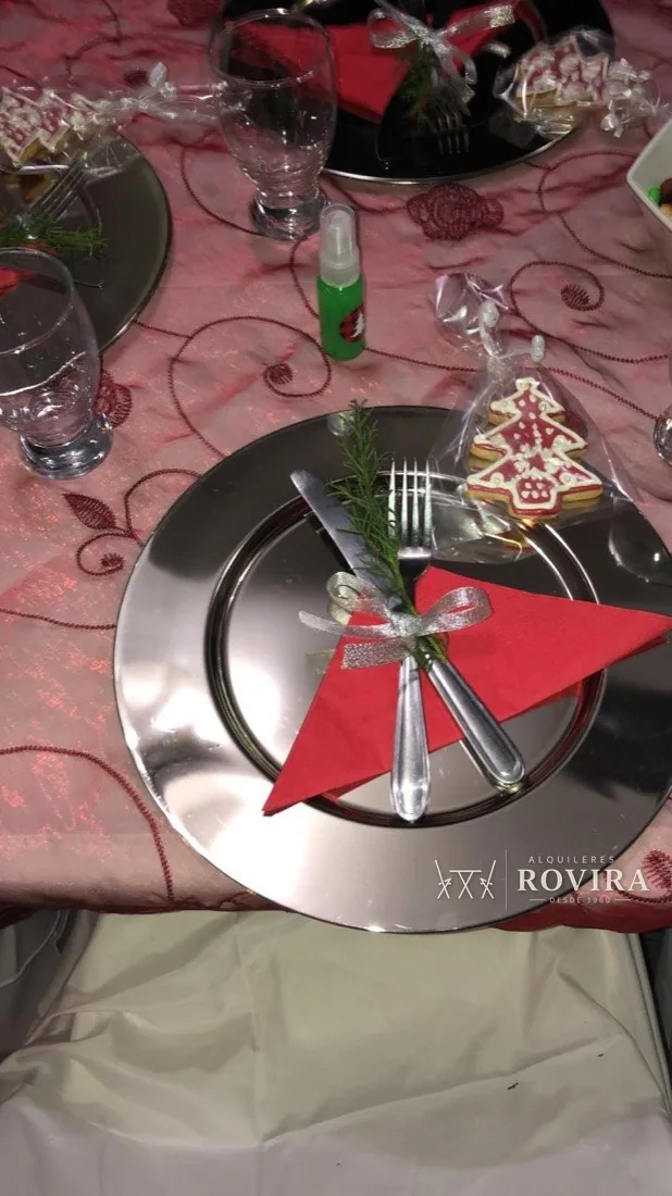 Plato base plateado con vajilla blanca, servilleta roja y galleta decorada, detalle de mesa