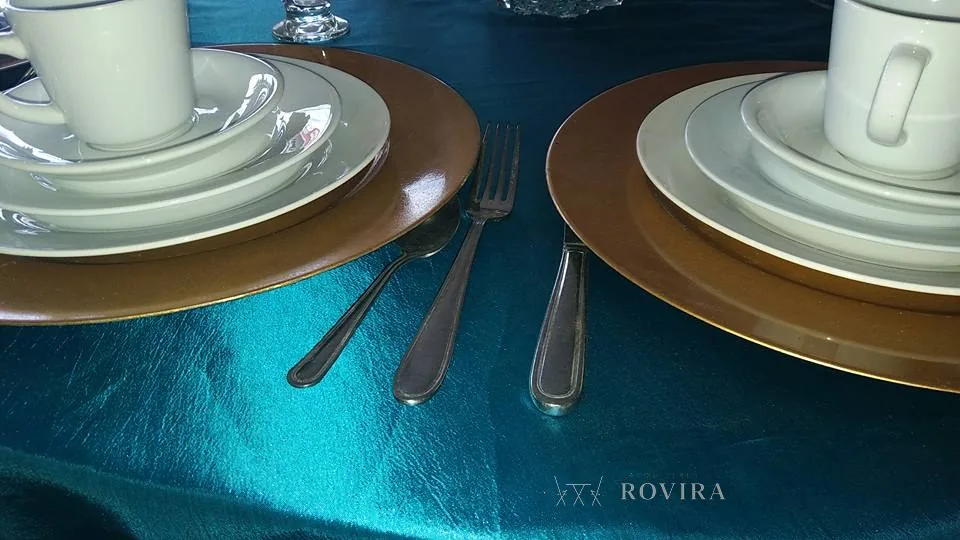 Puestos de mesa con plato base dorado sobre mantel turquesa satinado, cubiertos y tazas de café