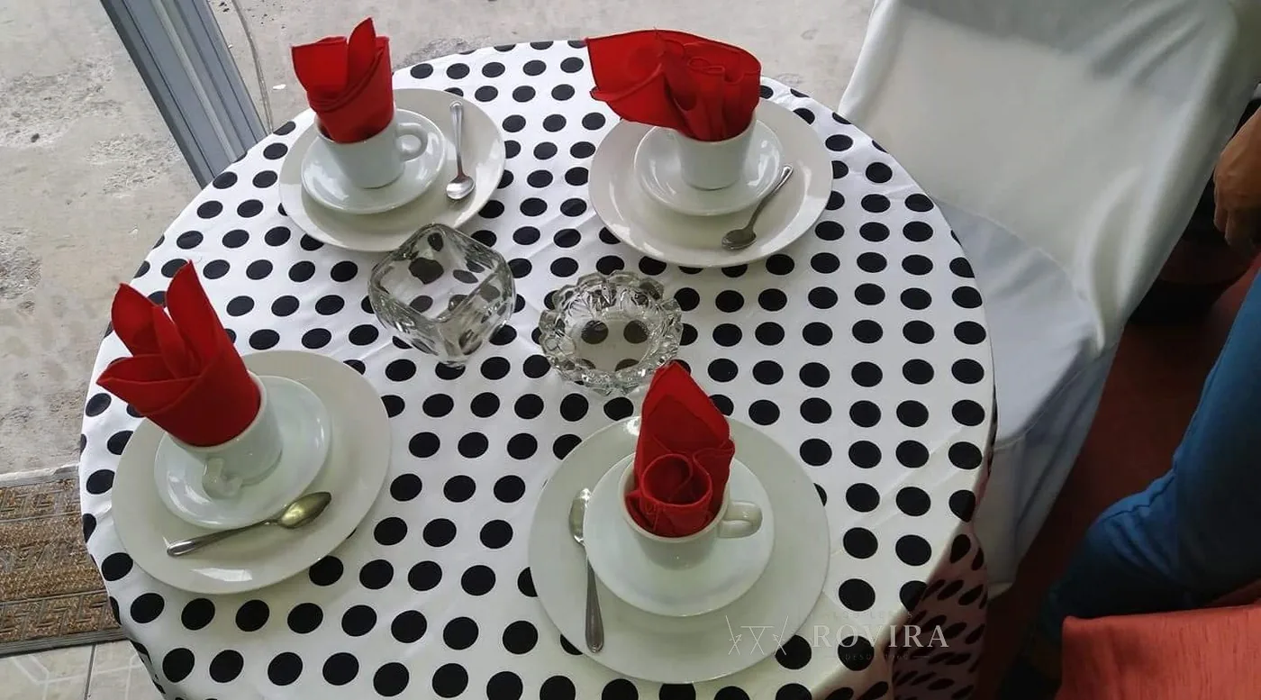 Mesa redonda con mantel de lunares blanco y negro, tazas de café y servilletas con rosa roja