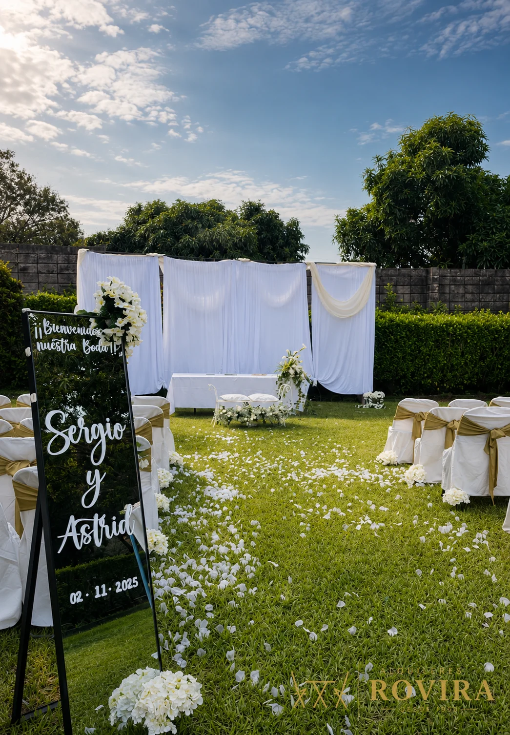Ceremonia de boda al aire libre con altar de tela blanca, sillas vestidas y camino de pétalos blancos sobre el césped