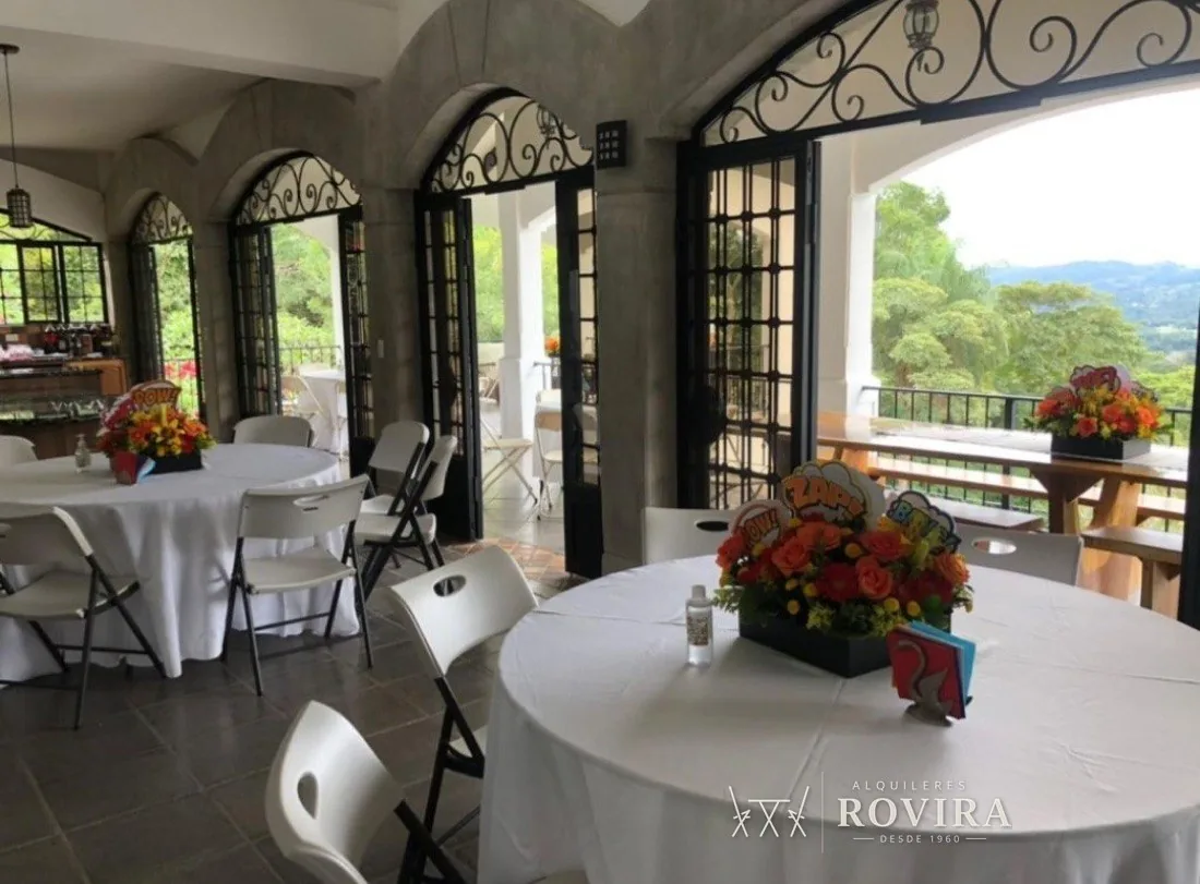 Villa con arquería de hierro y vista panorámica, montaje con sillas plegables blancas y negras