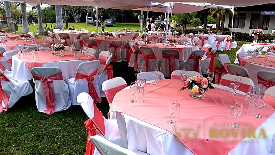 Mesas redondas con lazos rojos y rosados bajo toldo en jardín