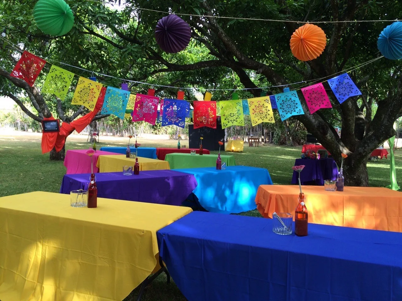 Fiesta típica costarricense al aire libre con papel picado de colores colgando entre los árboles y mesas vestidas, montaje producido por Alquileres Rovira